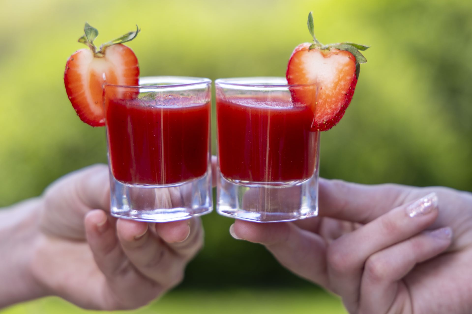 Zwei Erdbeer-Shots beim Anstoßen vor grüner Landschaft