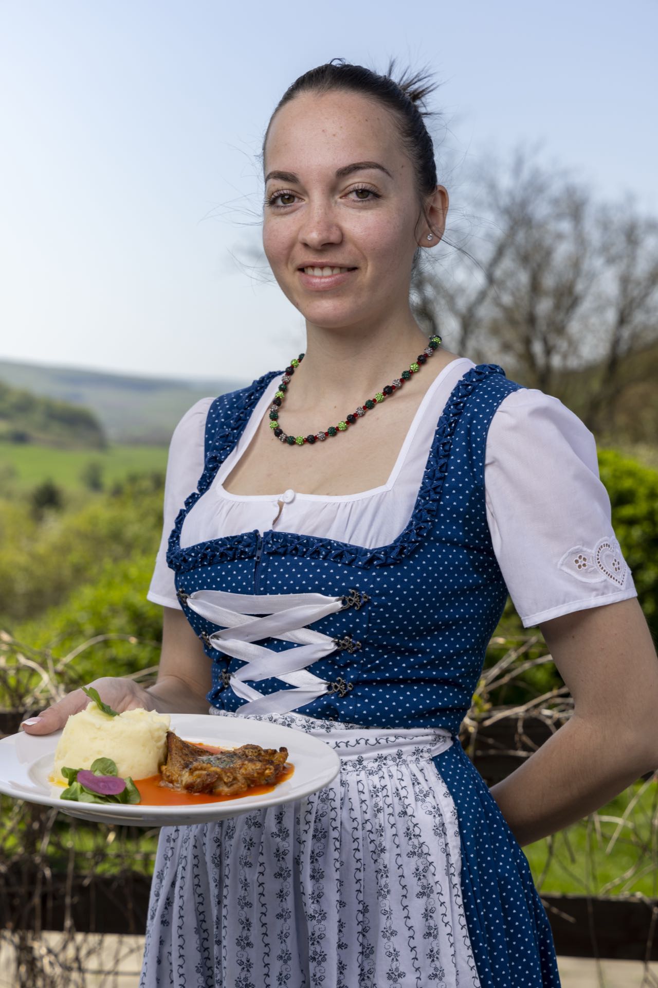 Kellnerin im Dirndl serviert Hauptgericht mit Kartoffelpüree