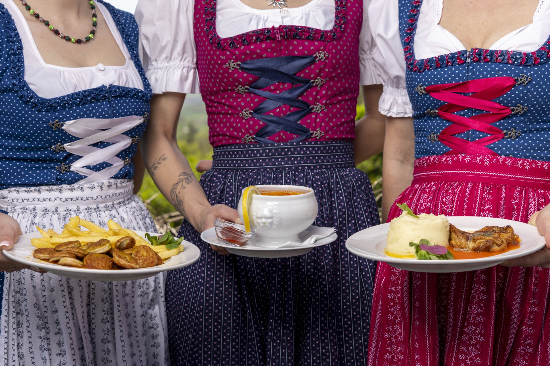 Drei Kellnerinnen im Dirndl servieren Schnitzel, Suppe und Hauptgericht
